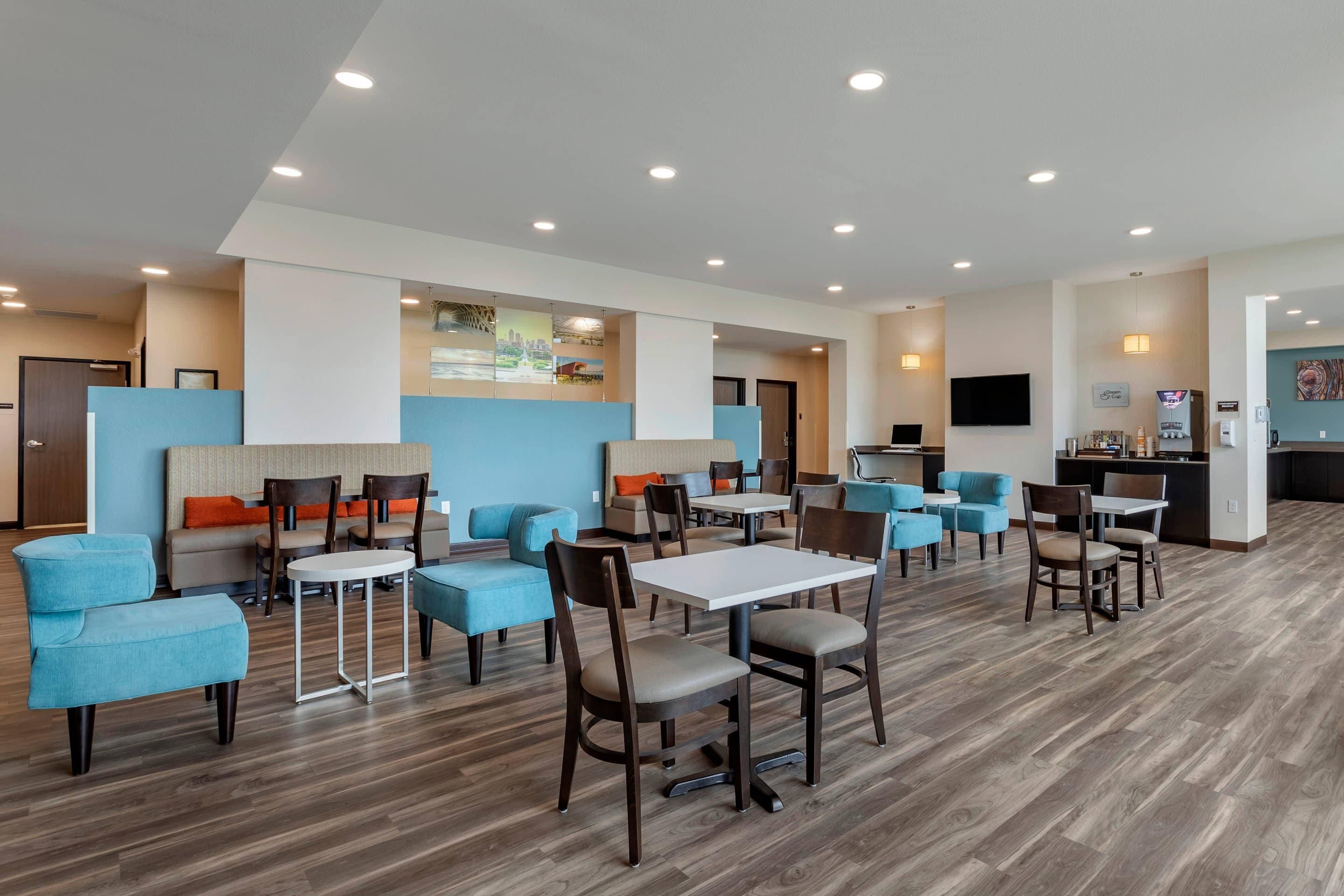 Een restaurantruimte in een hotel met meerdere tafels en stoelen, een keuken en een grote wand met kunstwerken.