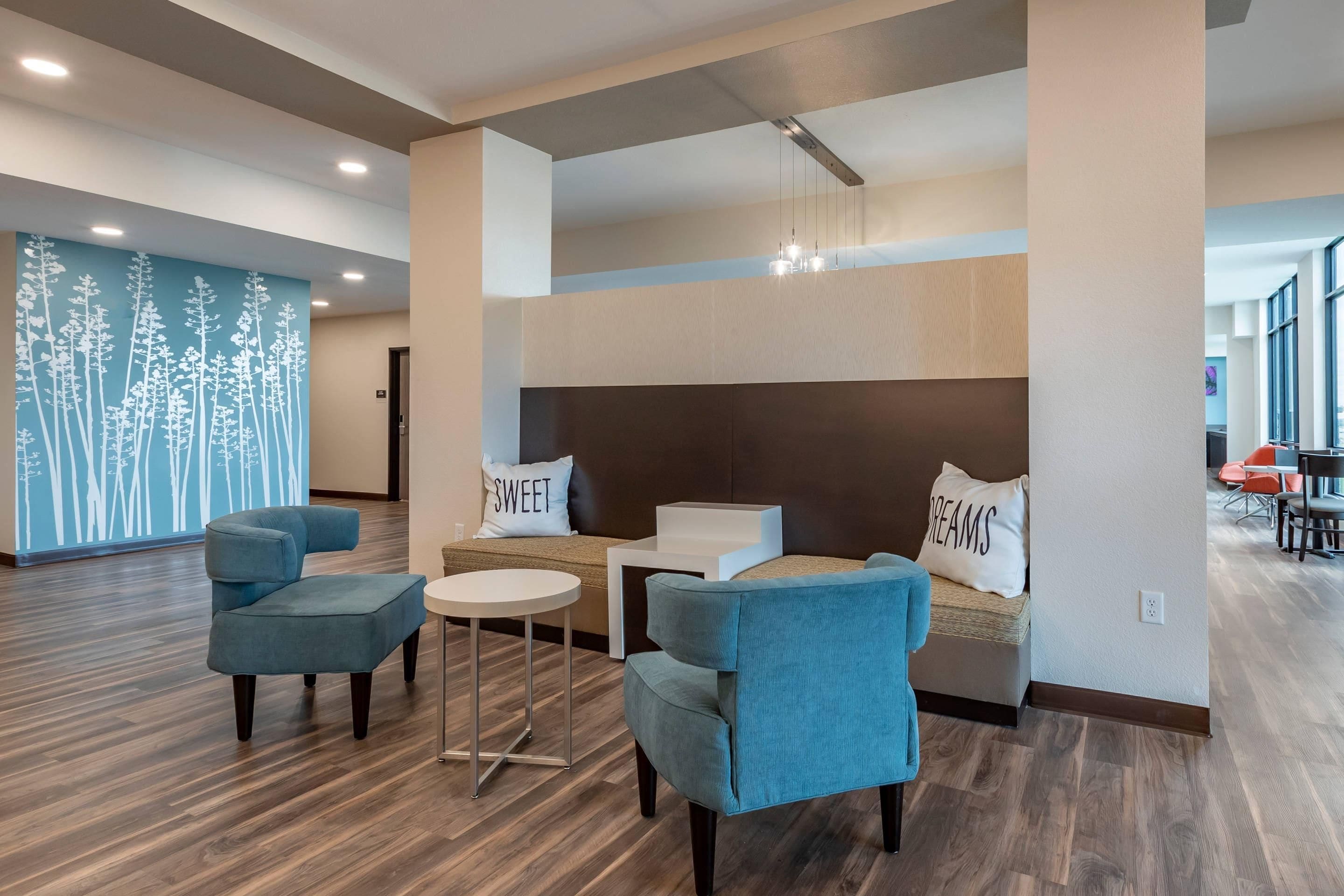 A hotel lobby with a seating area, a bed with pillows, and a wall with a tree design.
