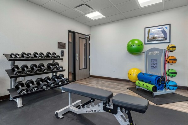 Une salle de sport équipée d’haltères, d’un banc, de ballons d’exercice et d’un appareil de fitness intelligent.