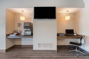 A modern hotel room with a flat-screen TV mounted on the wall, a coffee machine, a laptop, and a chair. - MainStay Suites Waukee - West Des Moines (Waukee)