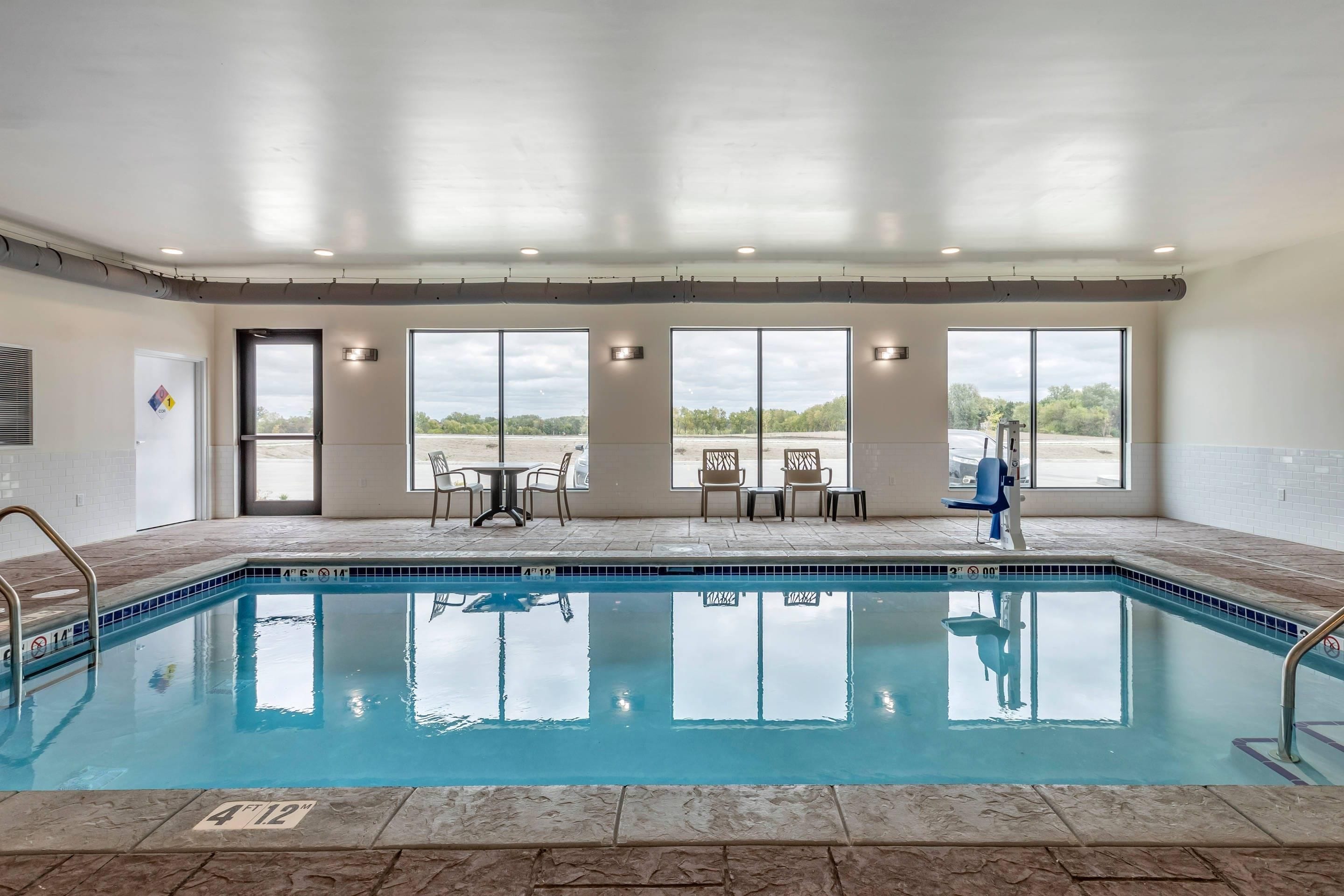Una piscina interior con paredes de vidrio transparente, suelo de baldosas y vistas al estacionamiento.