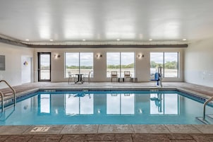 Una piscina interior con paredes de vidrio transparente, suelo de baldosas y vistas al estacionamiento.
