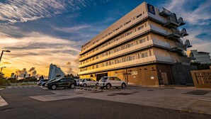Un hotel de varios pisos con diseño moderno, que cuenta con balcones en cada planta y un estacionamiento al frente.