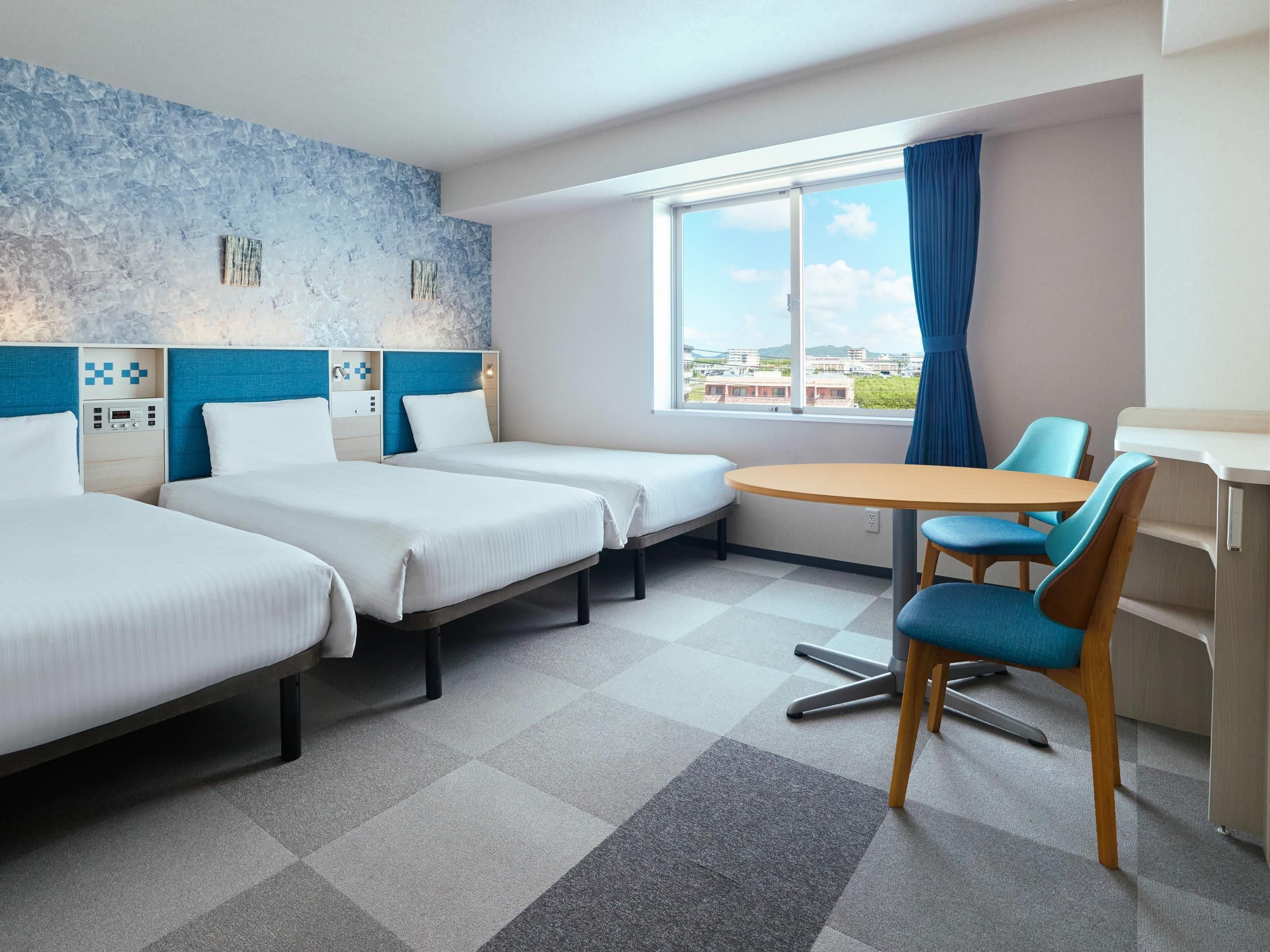 Hotellihuone, jossa on kaksi erillistä sänkyä, pieni pyöreä pöytä, tuoli ja ikkuna, josta on näkymä rakennuksiin.