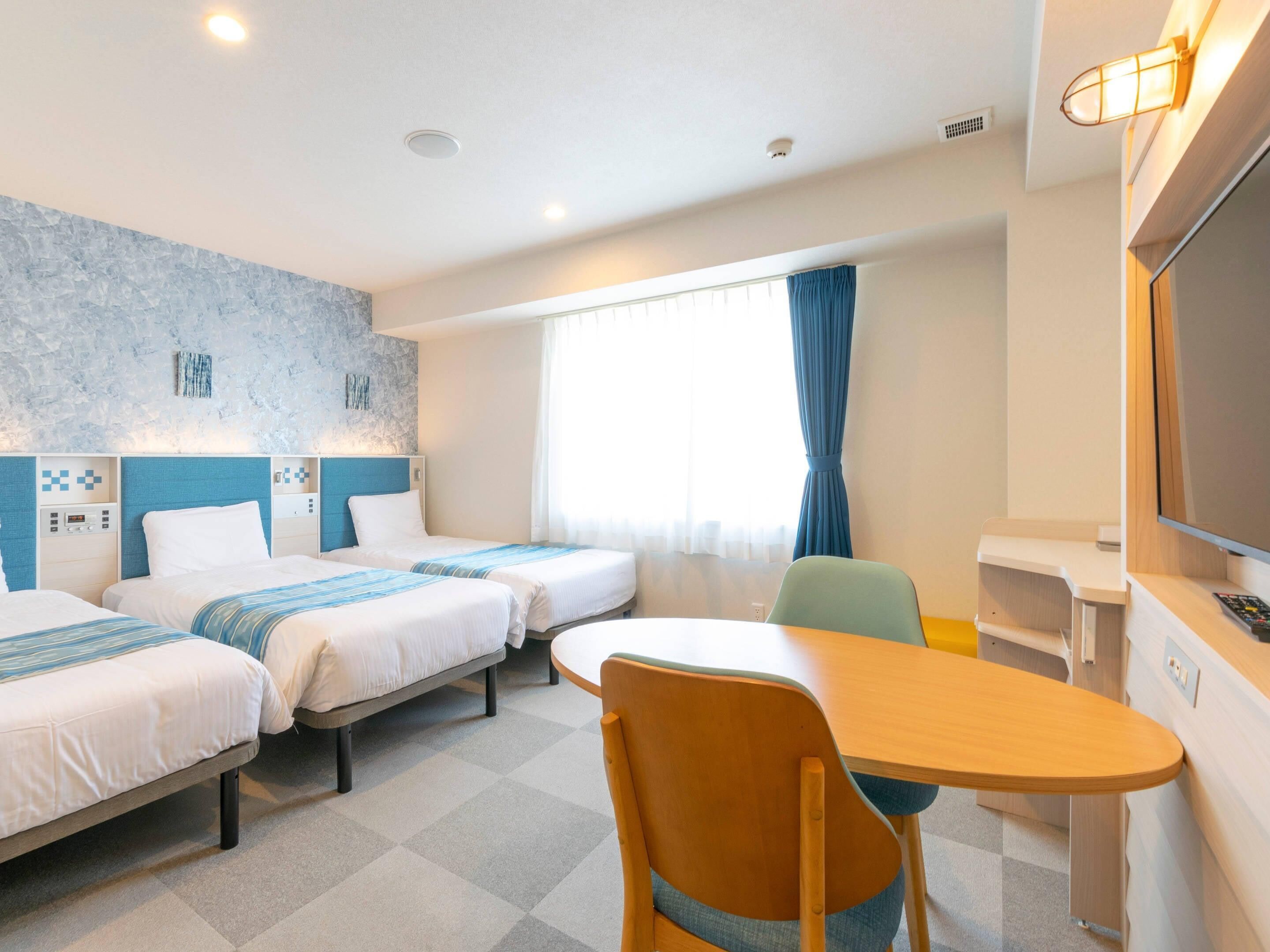 Habitación de hotel con dos camas, un escritorio, una silla, un televisor y una ventana con cortinas.