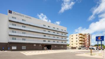 A multi-story Comfort Hotel with a flat facade, a parking lot, and a clear sky.