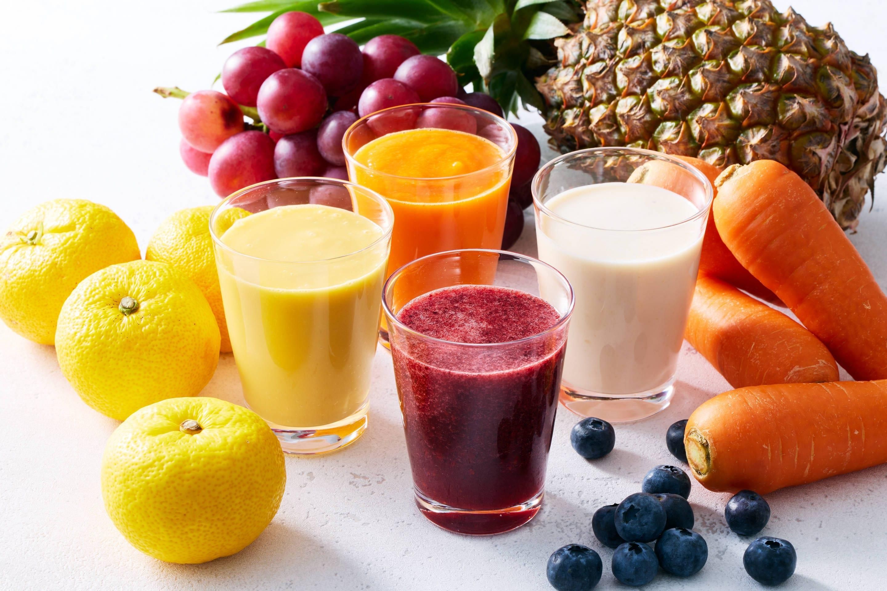 A variety of fresh fruits and vegetables, including lemons, grapes, pineapple, carrots, and blueberries, arranged on a surface.