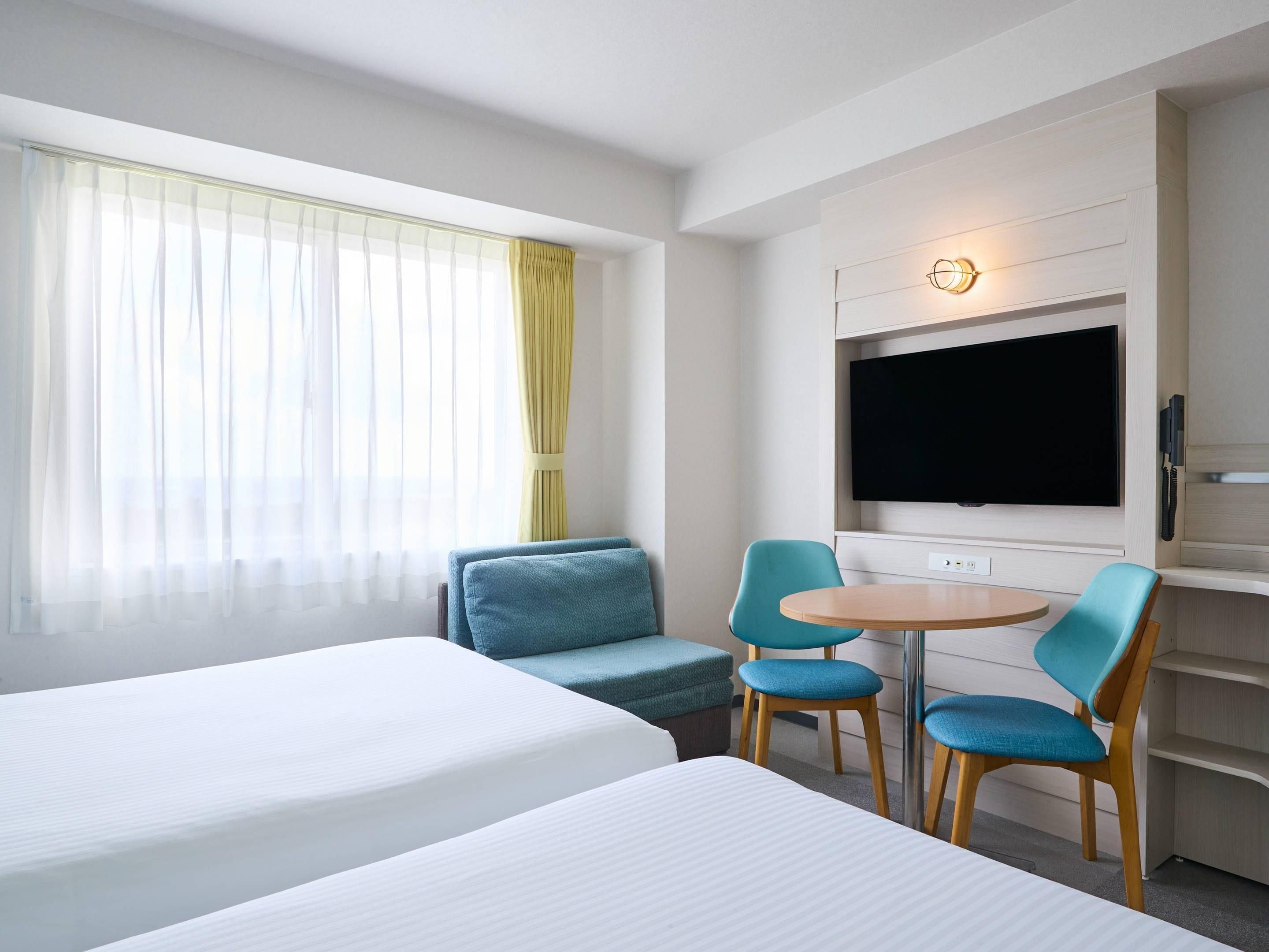A hotel room with two beds, a TV, and a seating area with chairs and a table.