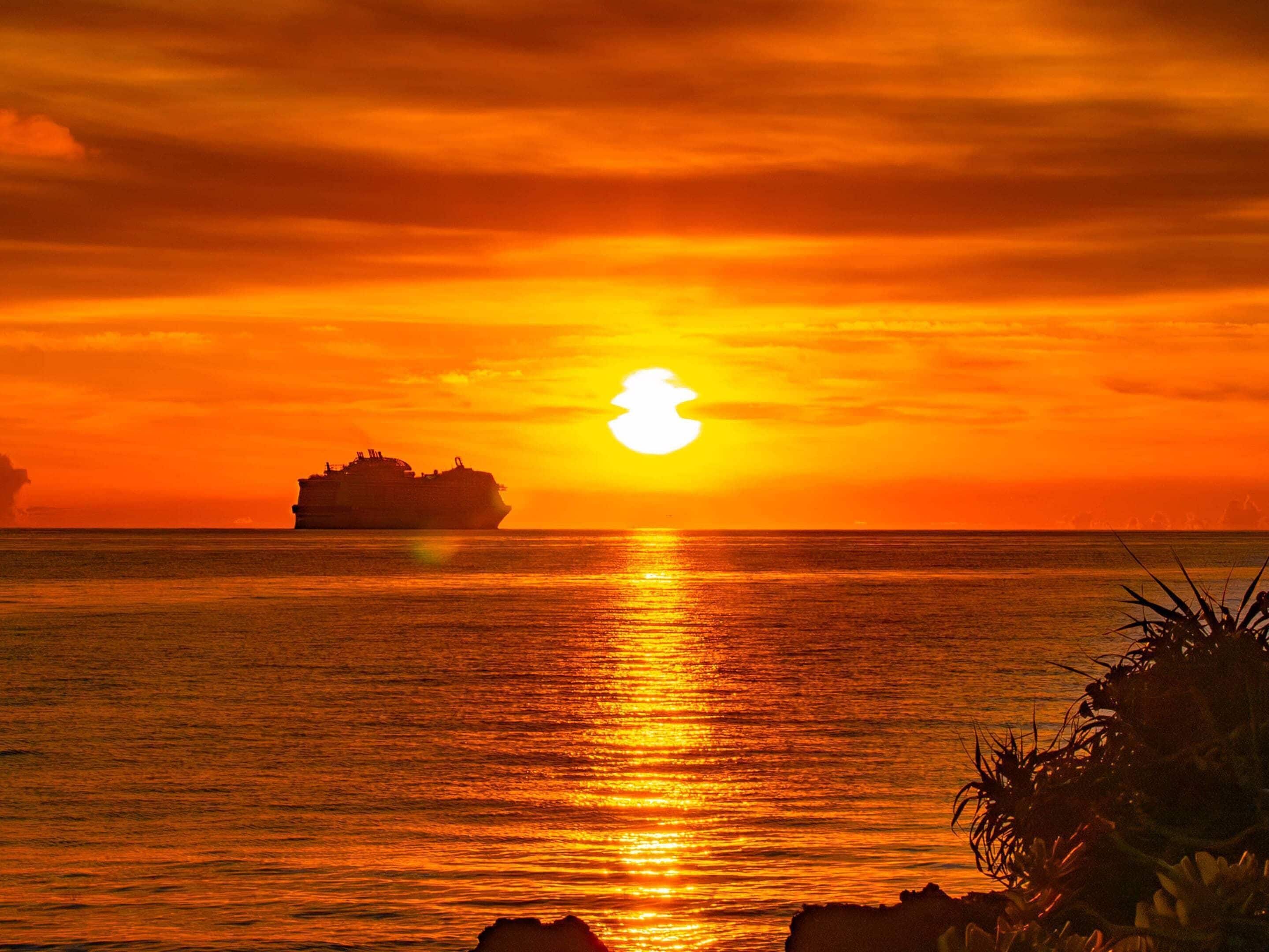A sunset over the ocean with a ship in the distance.