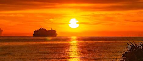 A sunset over the ocean with a ship in the distance.
