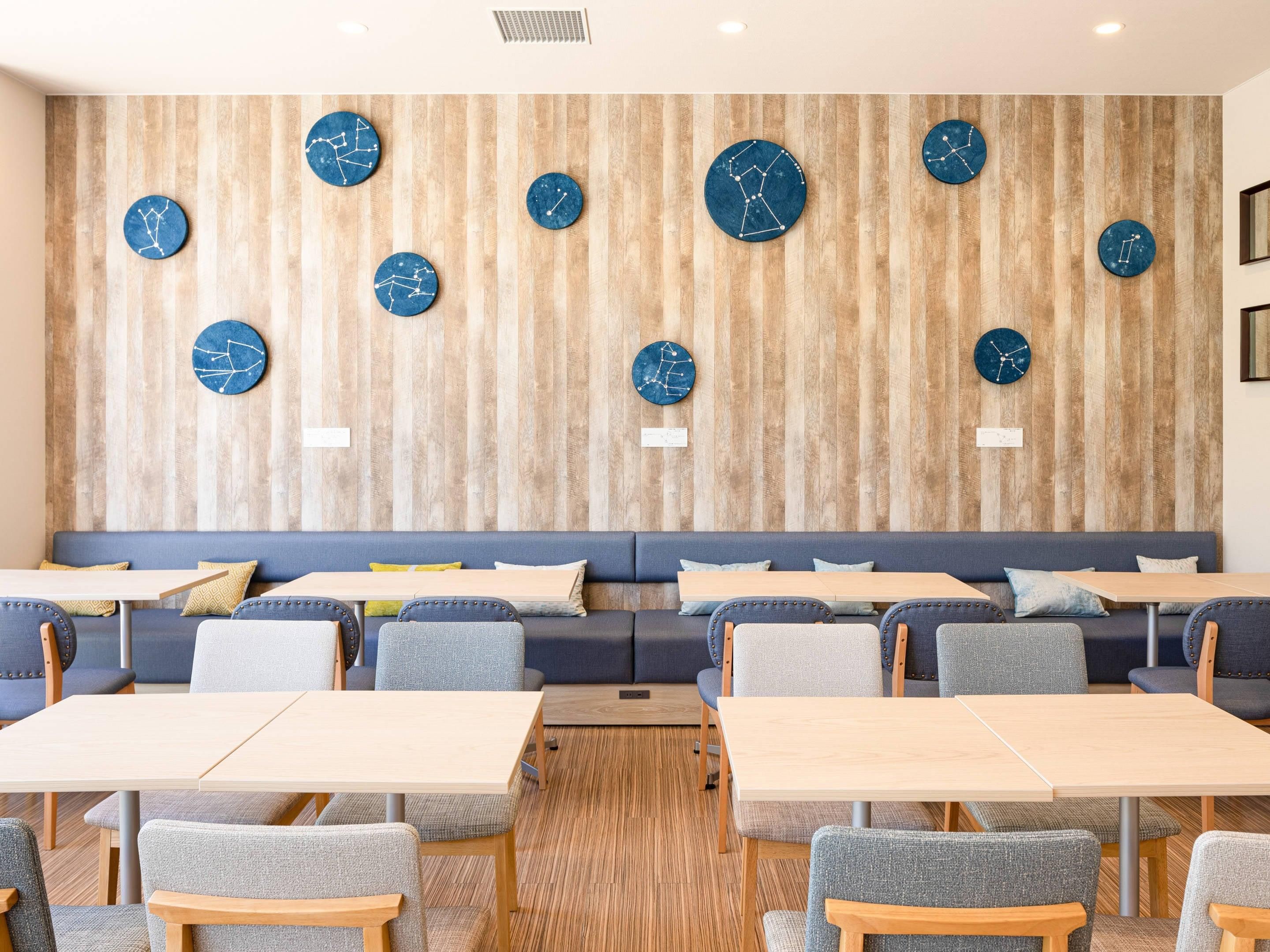 A modern dining area with wooden panel walls, round blue clocks, and a mix of grey and blue seating.