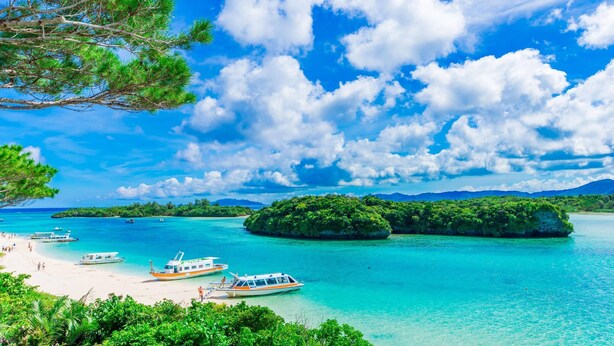 Una playa tropical con aguas turquesas cristalinas, embarcaciones y exuberante vegetación.