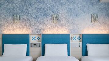 A hotel room with a textured blue wall, a bed with white bedding, and a control panel with a digital clock.