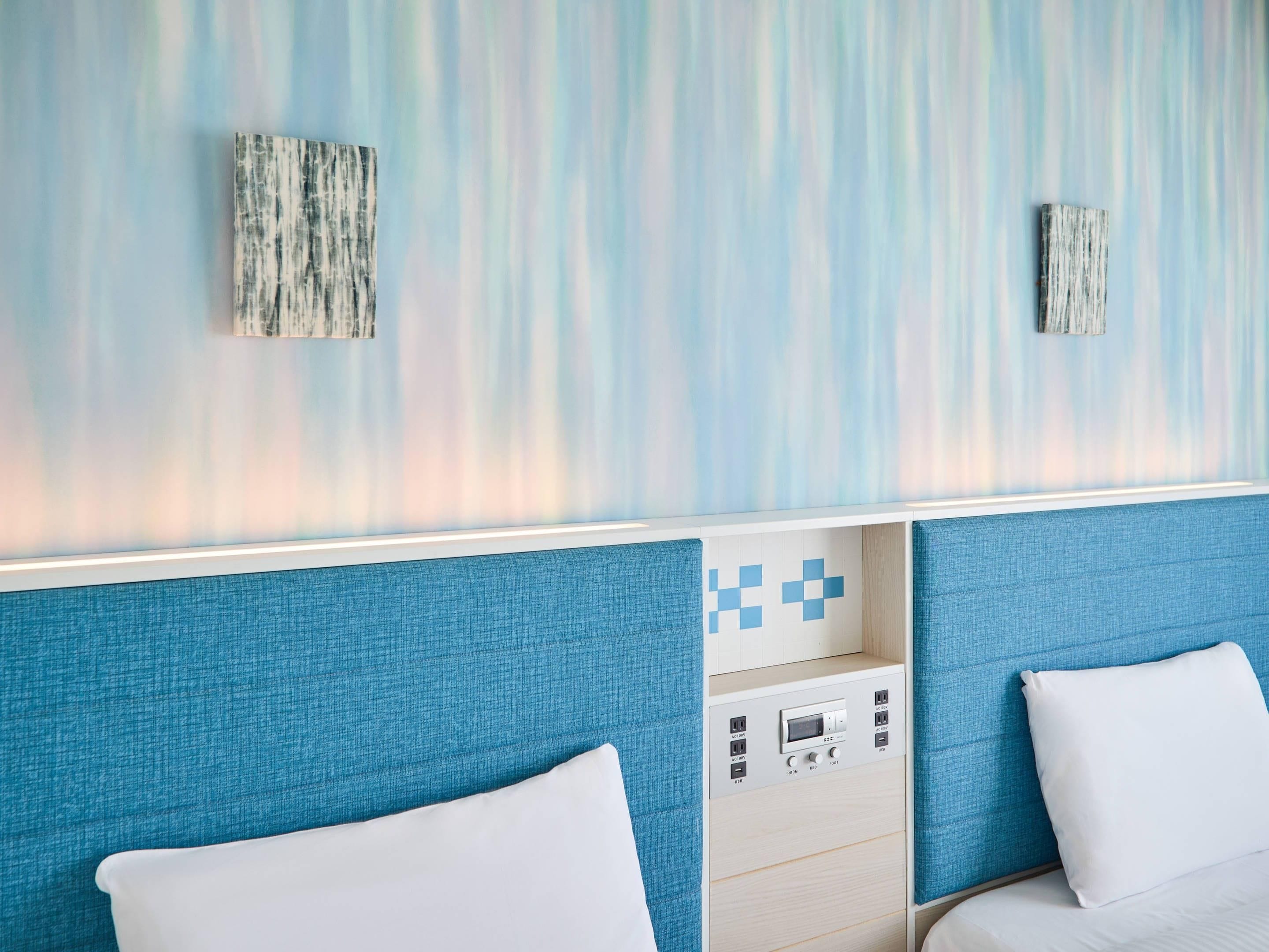 A hotel room with two beds, a control panel, and a textured wall.