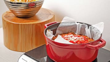 A red pot on a stove with a white label, a bowl of shredded vegetables, and a wooden cutting board.