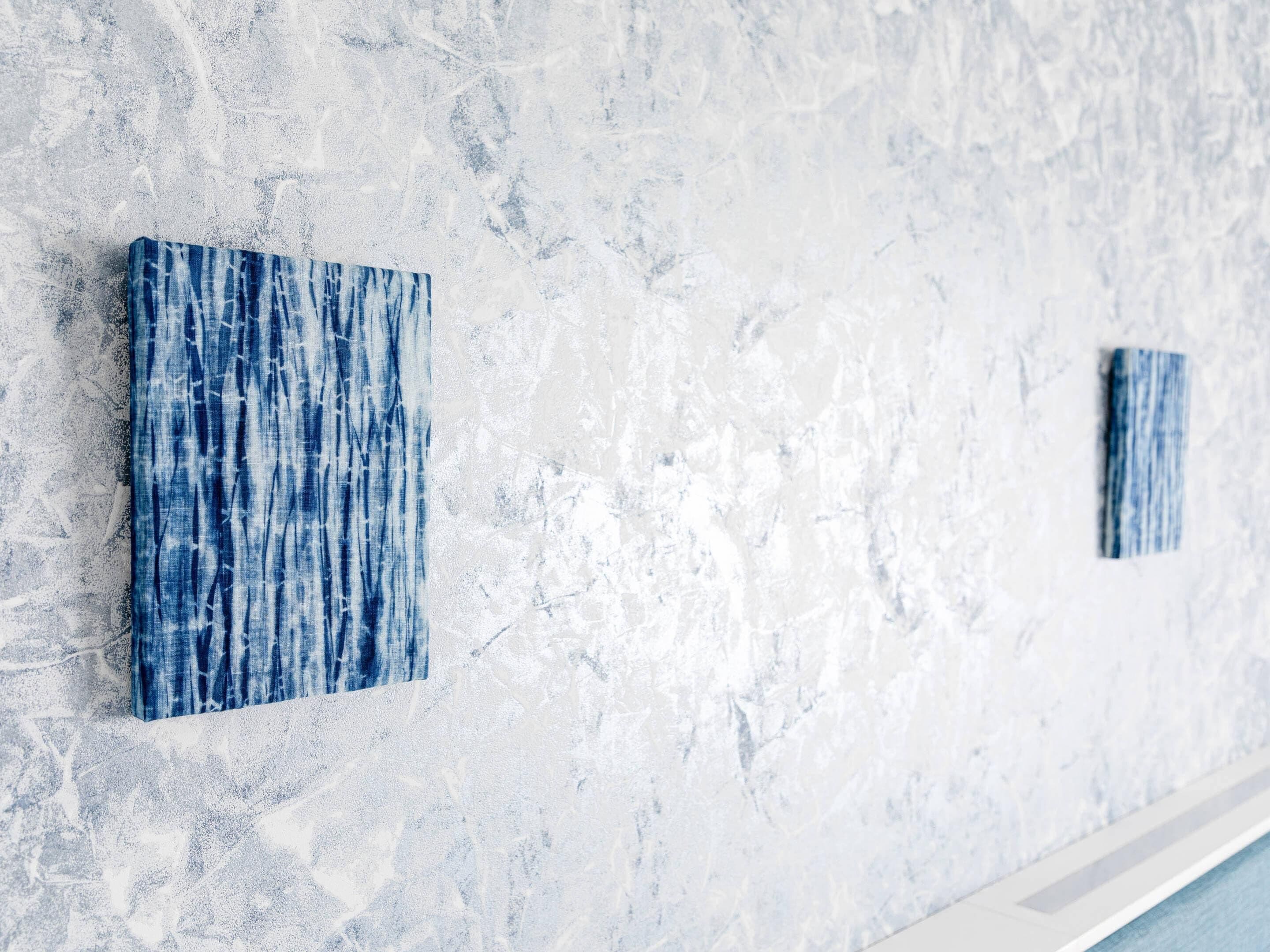 A wall with two square blue artworks.