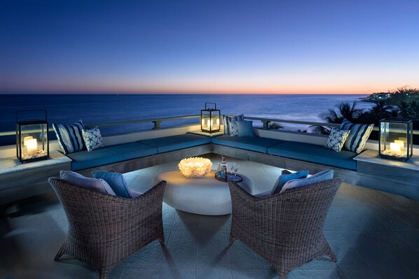 A sunset view from a balcony with wicker furniture and lanterns.