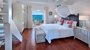 Une chambre avec un grand lit, une table de chevet, une commode, une fenêtre avec des rideaux et une vue sur la mer.