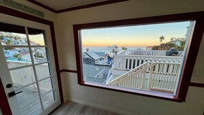 A room with a large window overlooking a deck and a view of the ocean at sunset. - Catalina Two Bedroom, Two Bath  View Home (Avalon)