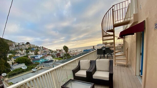 A balcony with wicker furniture, a glass table, and a view of a coastal town. - Catalina Two Bedroom, Two Bath  View Home (Avalon)
