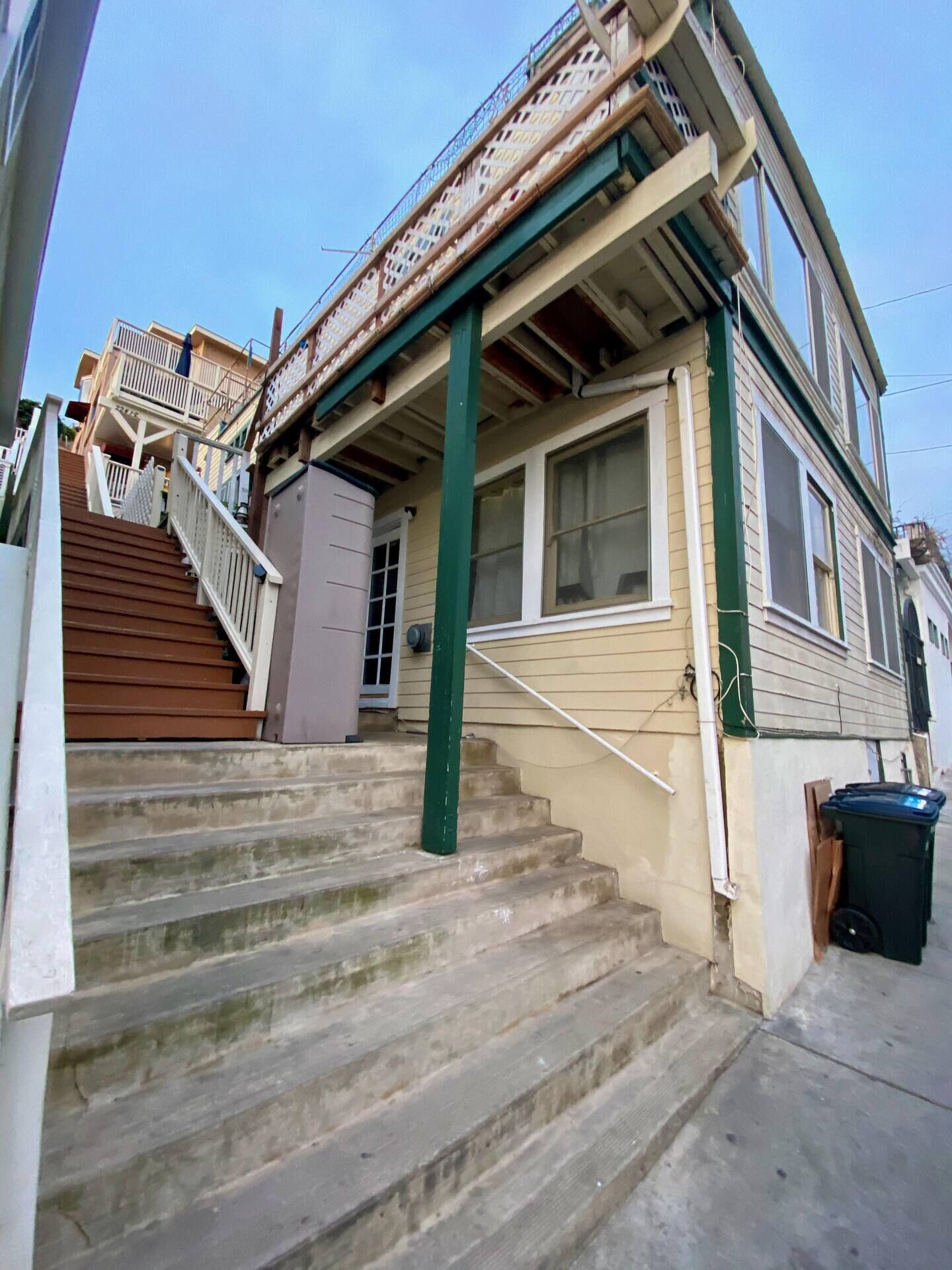 Une maison à deux étages avec un porche à l  ’avant, un escalier menant à l’entrée et une poubelle à l’extérieur.