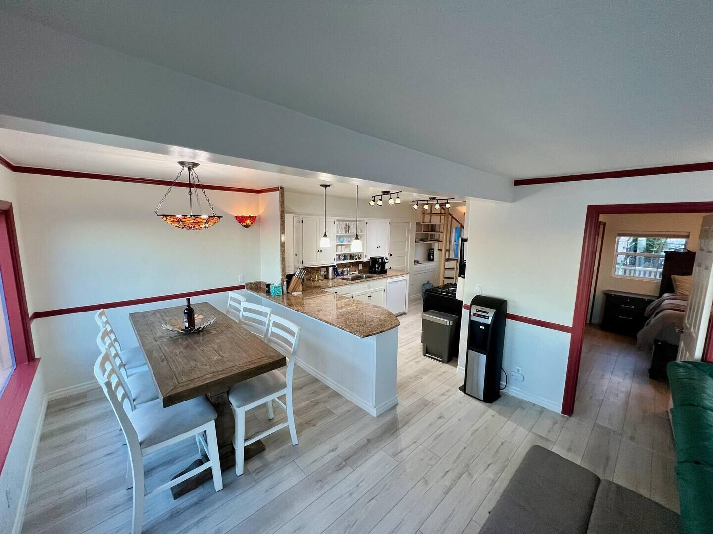 A modern kitchen with a central island, white cabinetry, and a dining area with a wooden table and white chairs.