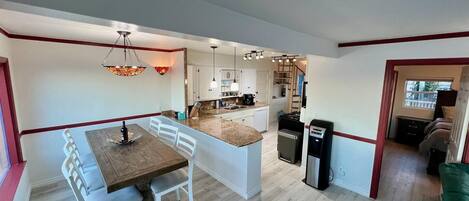 A modern kitchen with a central island, white cabinetry, and a dining area with a wooden table and white chairs.