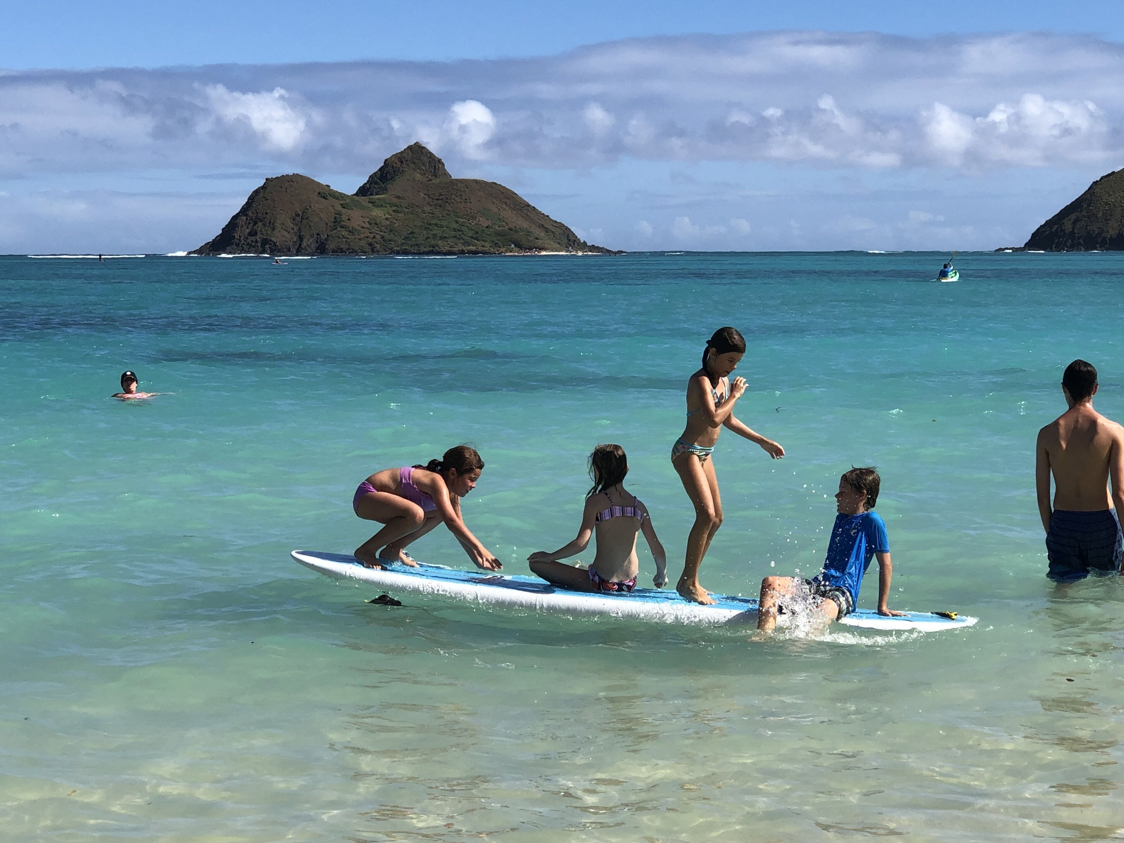 A group of people in a clear blue sea with a mountainous island in the background.