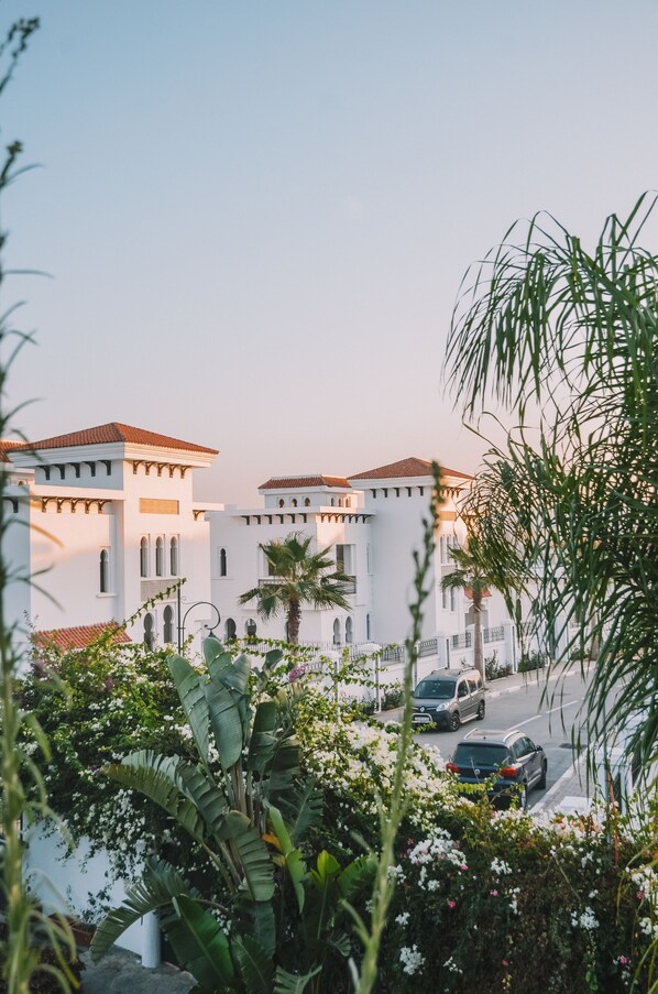 A white building with a red-tiled roof, surrounded by lush greenery and parked cars. - Dar Tanja (Tangier)