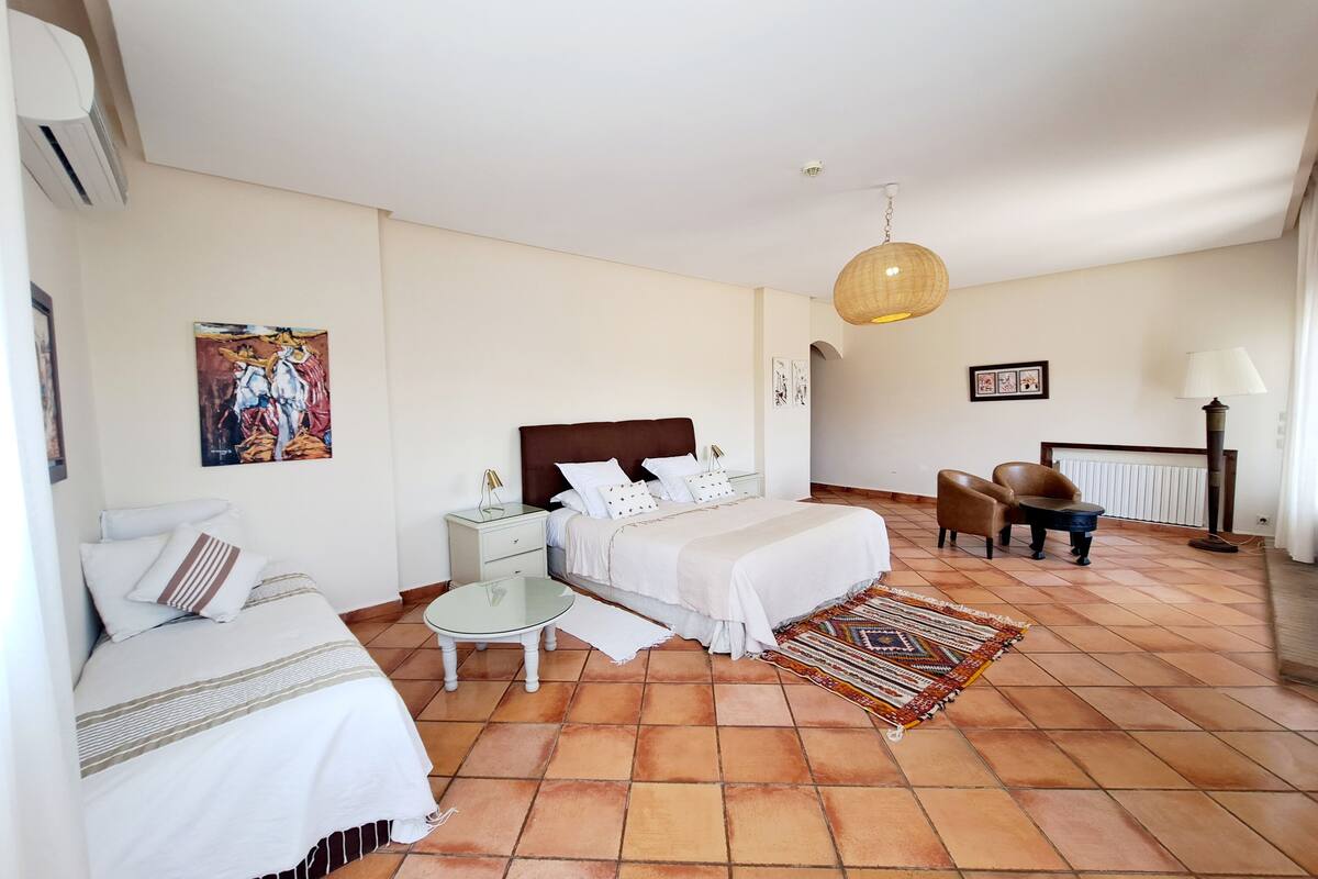 A bedroom with a bed, bedside table, lamp, chair, and artwork.