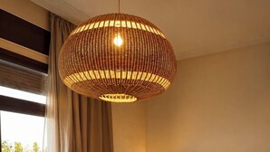 Hotellihuone, jossa on sänky, riippuvalaisin, yöpöytä, seinään kiinnitetty lamppu ja näkymä ulkoalueelle.