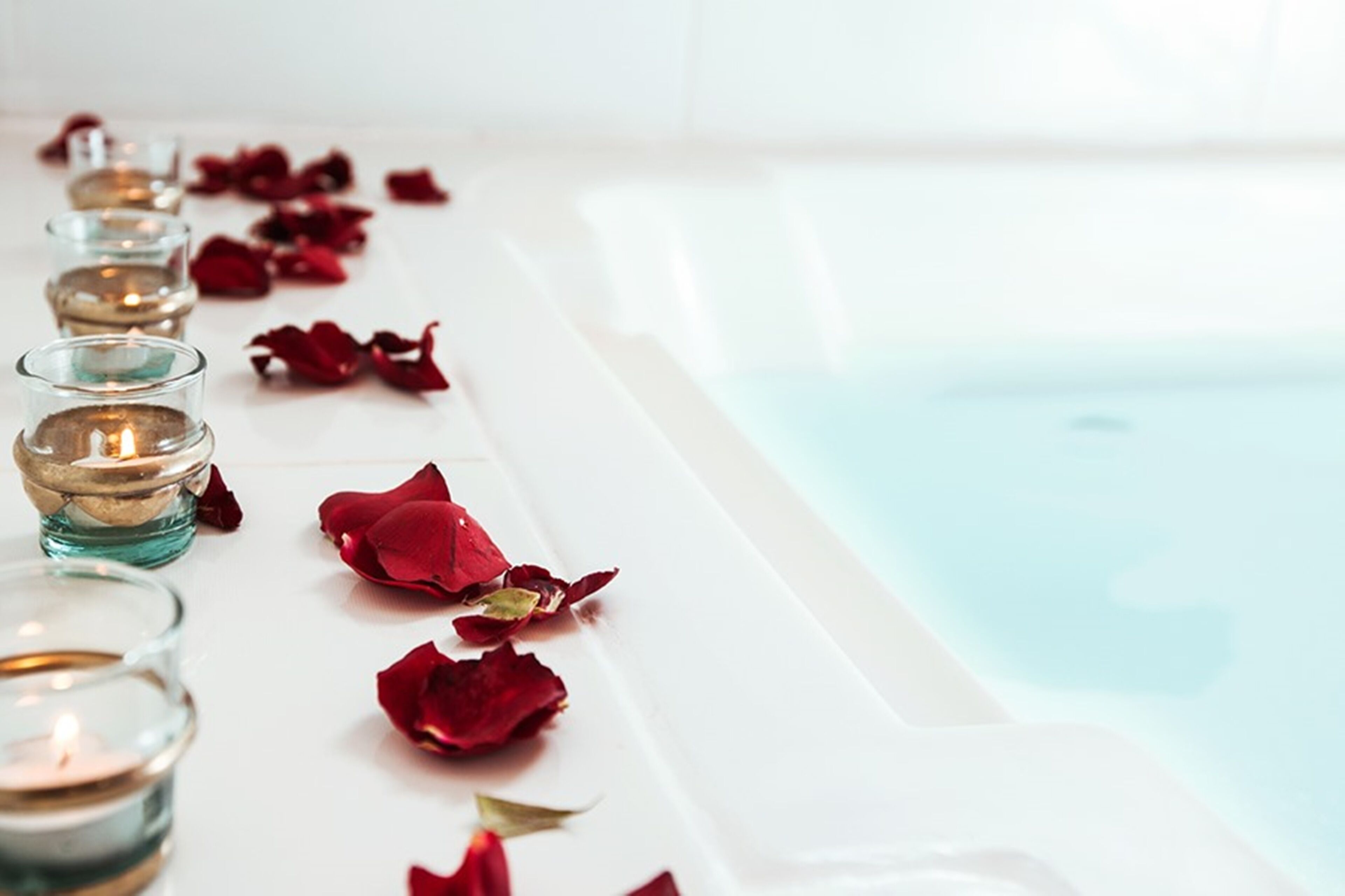 A row of candles and rose petals on a bathtub.