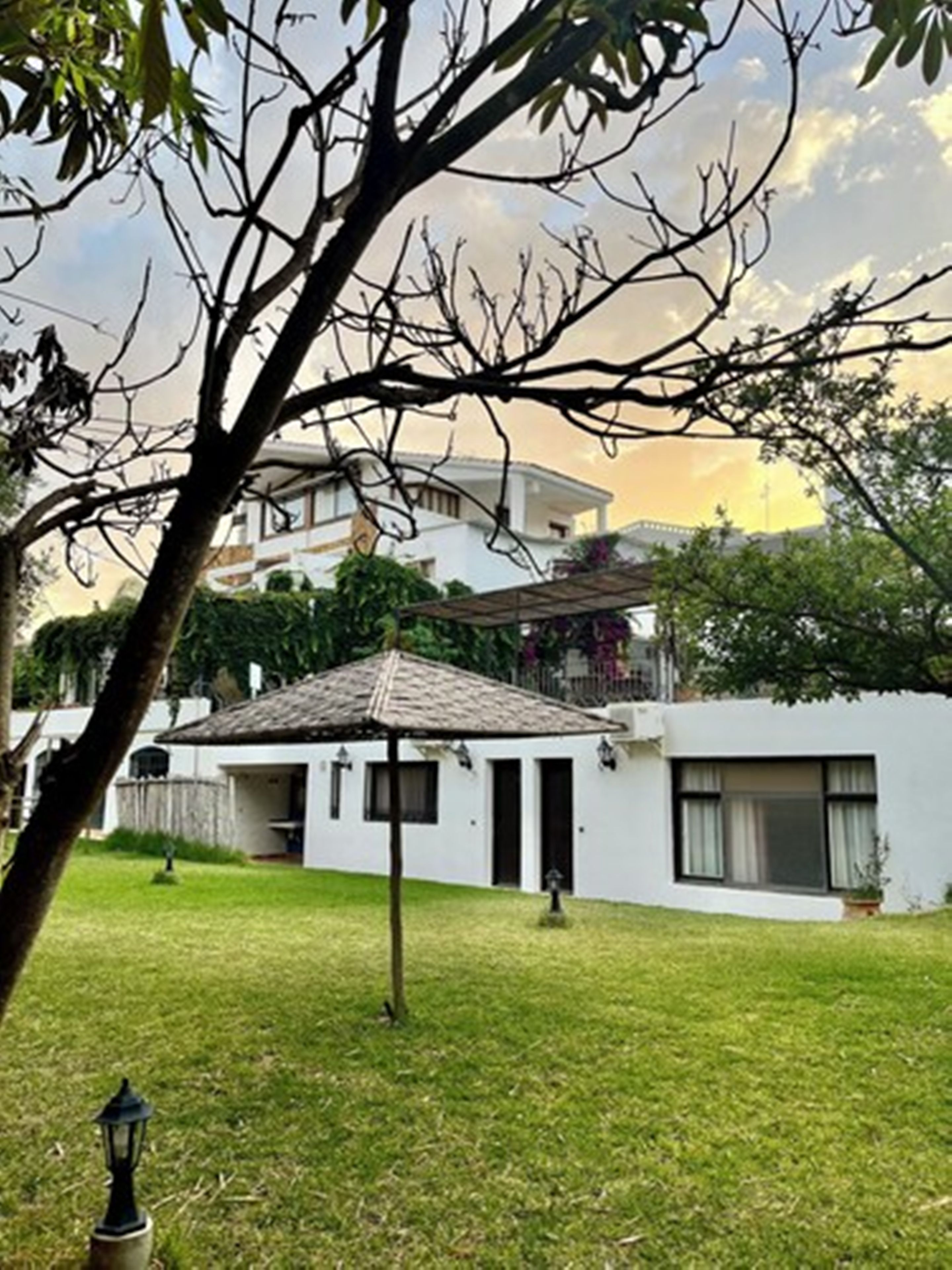 Un quartier résidentiel avec une maison blanche, un petit kiosque et un arbre au premier plan.