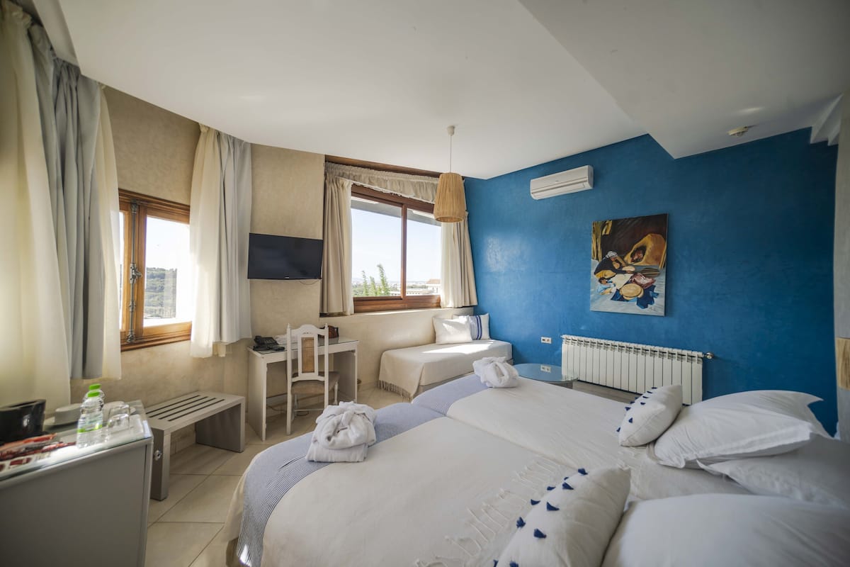A hotel room with two beds, a desk, a chair, and a window with curtains.