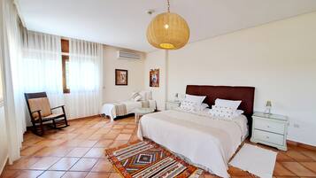 Ein helles Schlafzimmer mit einem großen Bett, einem Schaukelstuhl, einem gemusterten Teppich und einer Hängeleuchte.