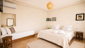 Habitación de hotel con cama, mesita de noche, taburete de madera, alfombra grande tejida y lámpara en el techo.