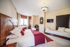 Une chambre d’hôtel avec un grand lit, un lit plus petit, une télévision et un miroir décoratif.