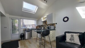 Eine kompakte Küche mit Mikrowelle, Spüle und Fenster. Ein schwarzes Ledersofa mit Kissen und ein kleiner Teppich liegen auf dem Boden.