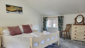 Ein Schlafzimmer mit Bett, Schminktisch, Stuhl, Fenster mit Vorhängen und einem Bild an der Wand.