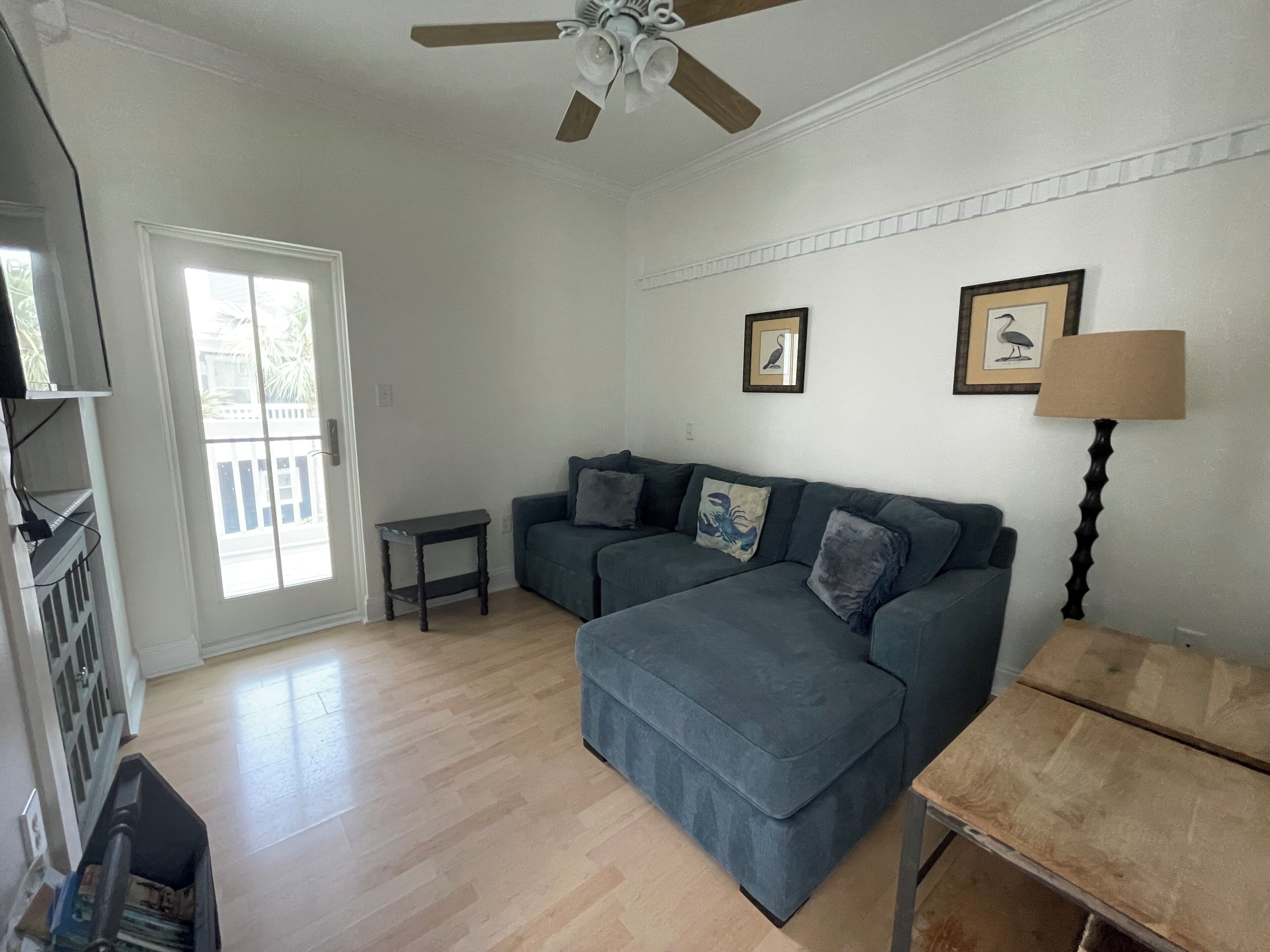 A living room with a sofa, a small table, a ceiling fan, and a door leading outside.
