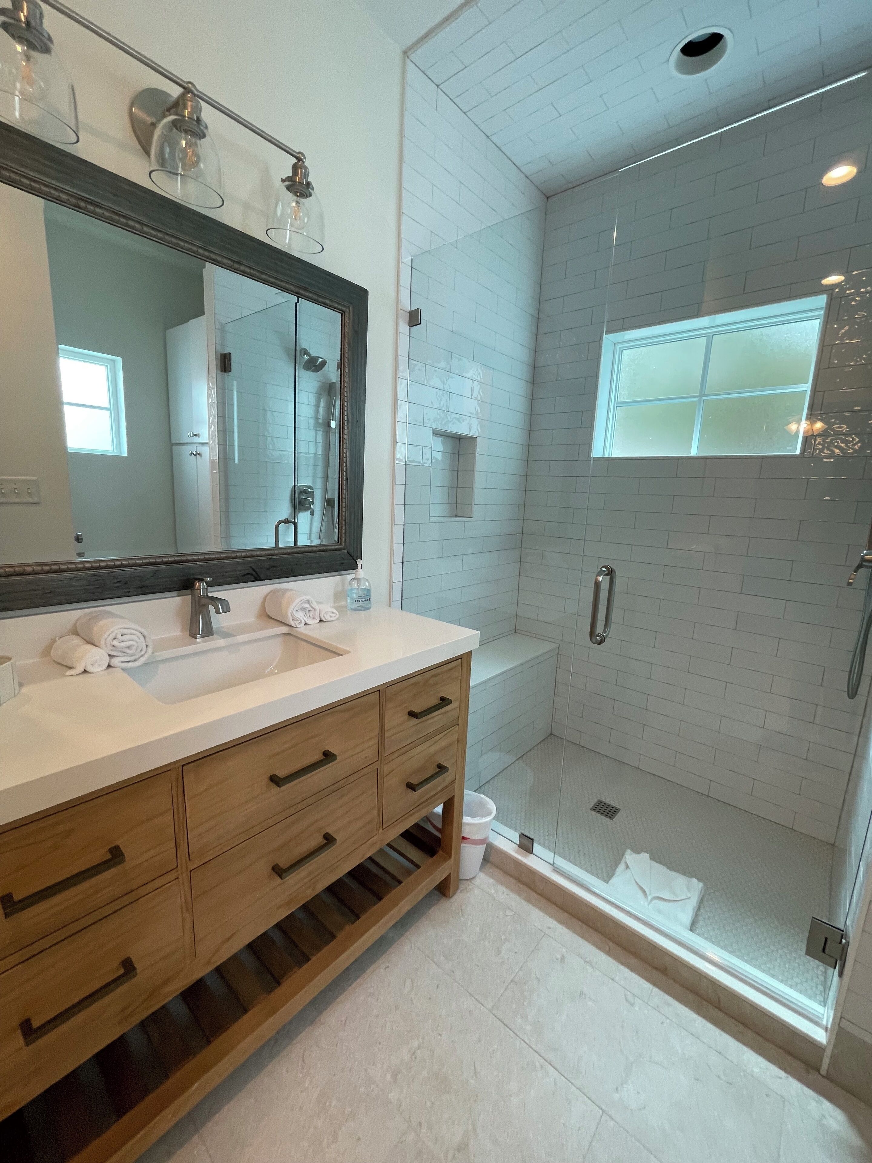A modern bathroom with a large mirror, dual sinks, and a walk-in shower.