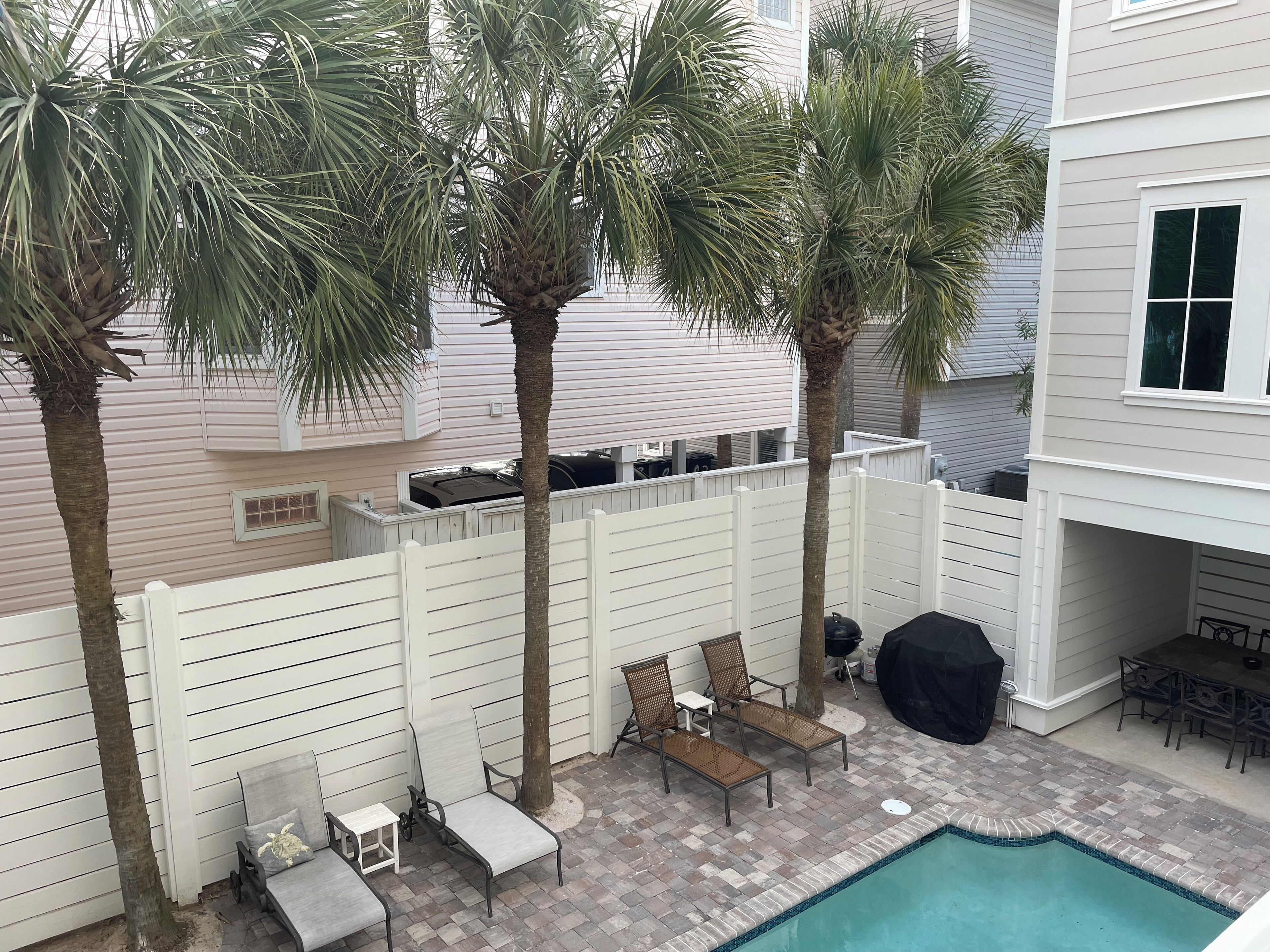 A backyard with a pool, palm trees, and outdoor furniture.