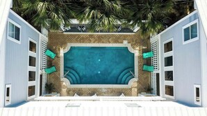 Une piscine rectangulaire dotée d’une terrasse carrelée, entourée d’une clôture et de palmiers.