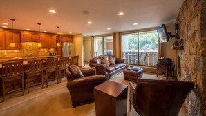 A spacious living area with a kitchen, wooden furniture, and a stone wall. - Scorpio Condos with Great Vail Mountain Views by RedAwning (Vail)