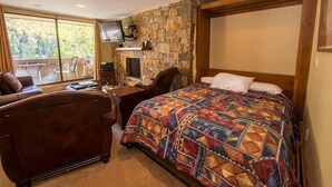 A bedroom with a large bed, a desk, a chair, a TV, and a stone wall. - Scorpio Condos with Great Vail Mountain Views by RedAwning (Vail)