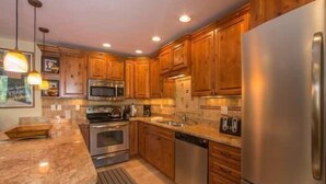 A kitchen with wooden cabinets, stainless steel appliances, granite countertops, and pendant lighting. - Scorpio Condos with Great Vail Mountain Views by RedAwning (Vail)