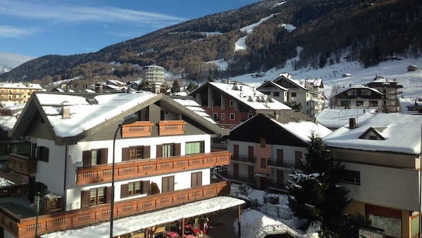 Eine verschneite Bergstadt mit mehrstöckigen Gebäuden, Skipisten und blauem Himmel.