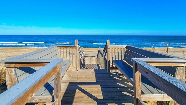Une promenade en bois menant à la plage, d’où l’on a une vue dégagée sur l’océan.