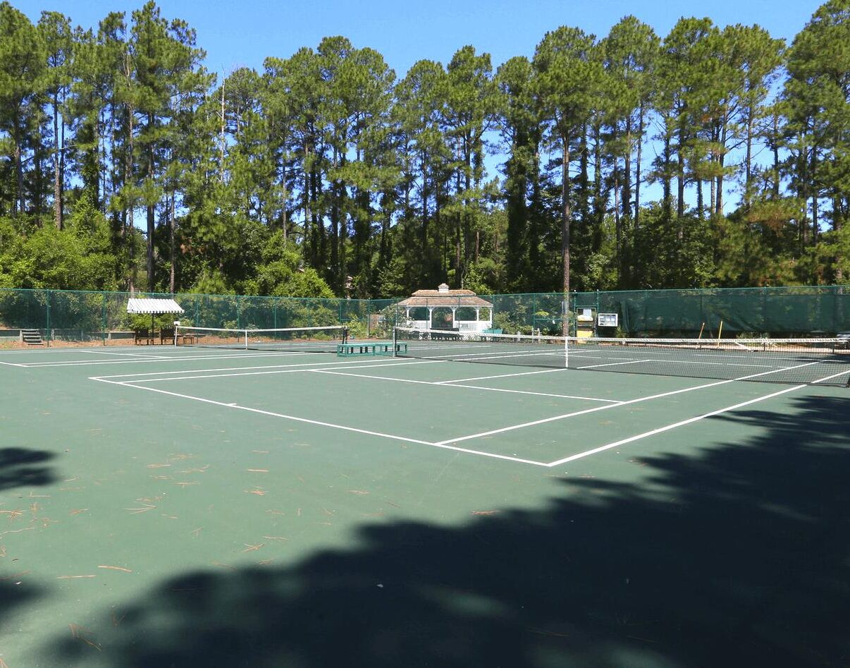 Una cancha de tenis con un pabellón, rodeada de árboles altos.
