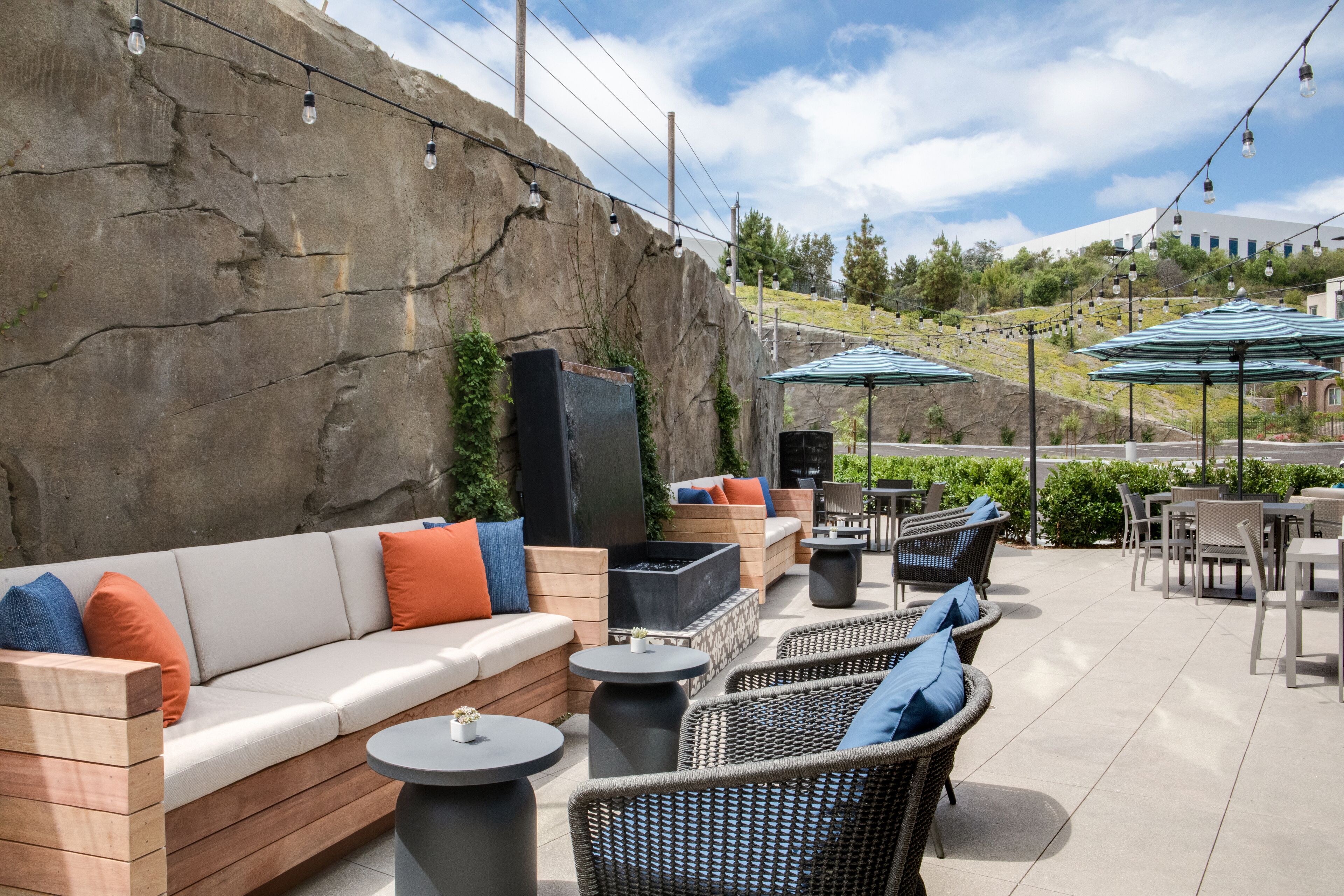 Un patio exterior con sofá, sillas, mesas y sombrillas.
